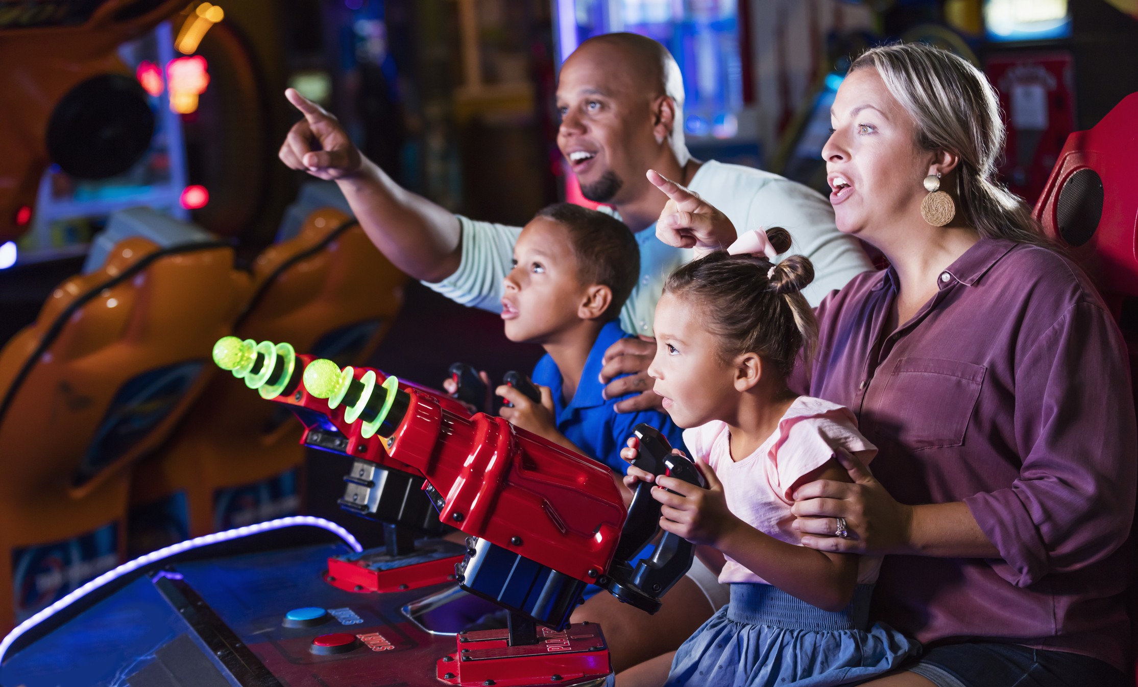 Children play arcade games, and mother and father point and teach their two children how to play the game in Mr. Gatti's Pizza franchise with the arcade games and ordering system.