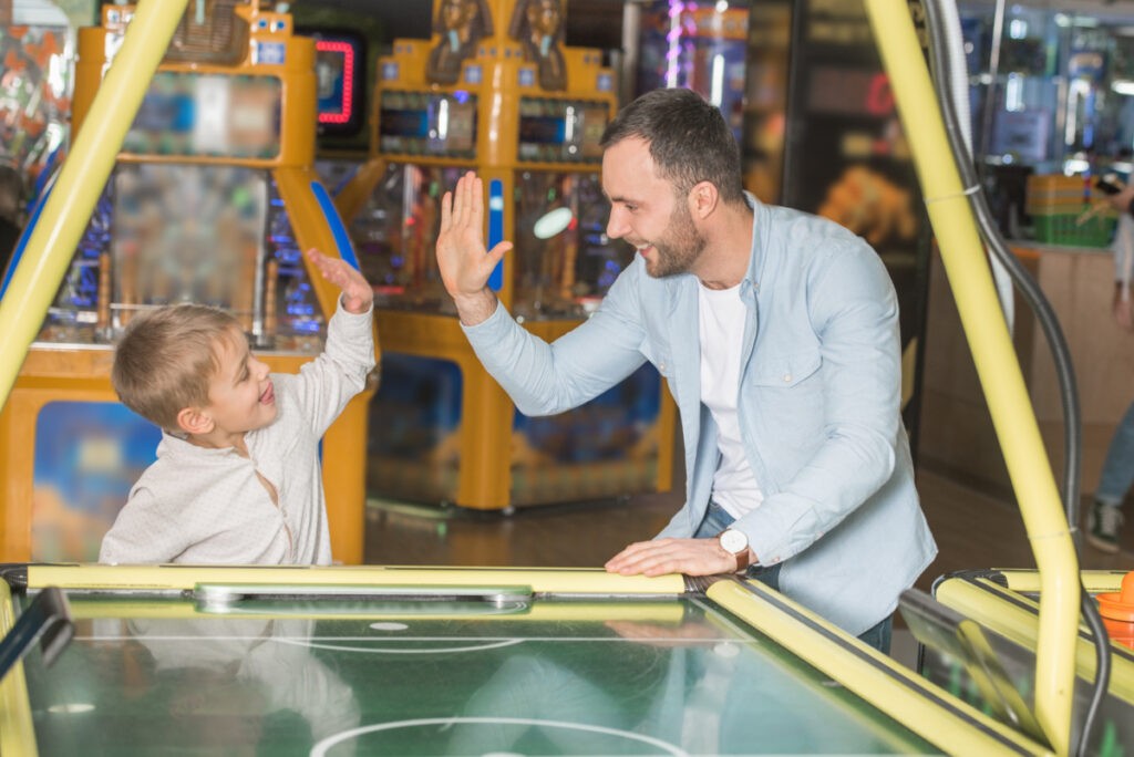 happy father and son giving high five while playing air hockey in family entertainment center